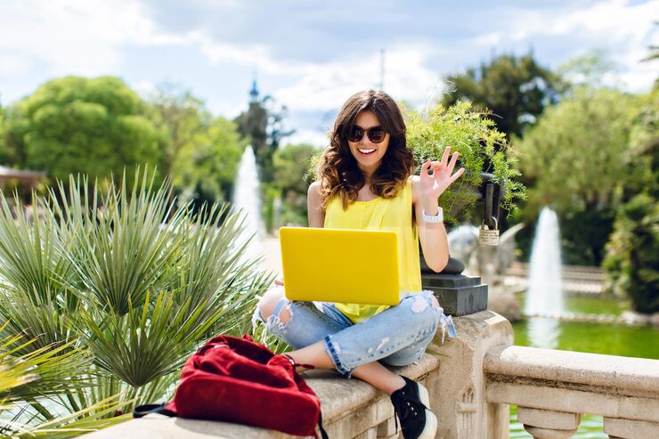 brunette girl sunglasses is sitting fence park she holds yellow laptop smiling camera 197531 25034